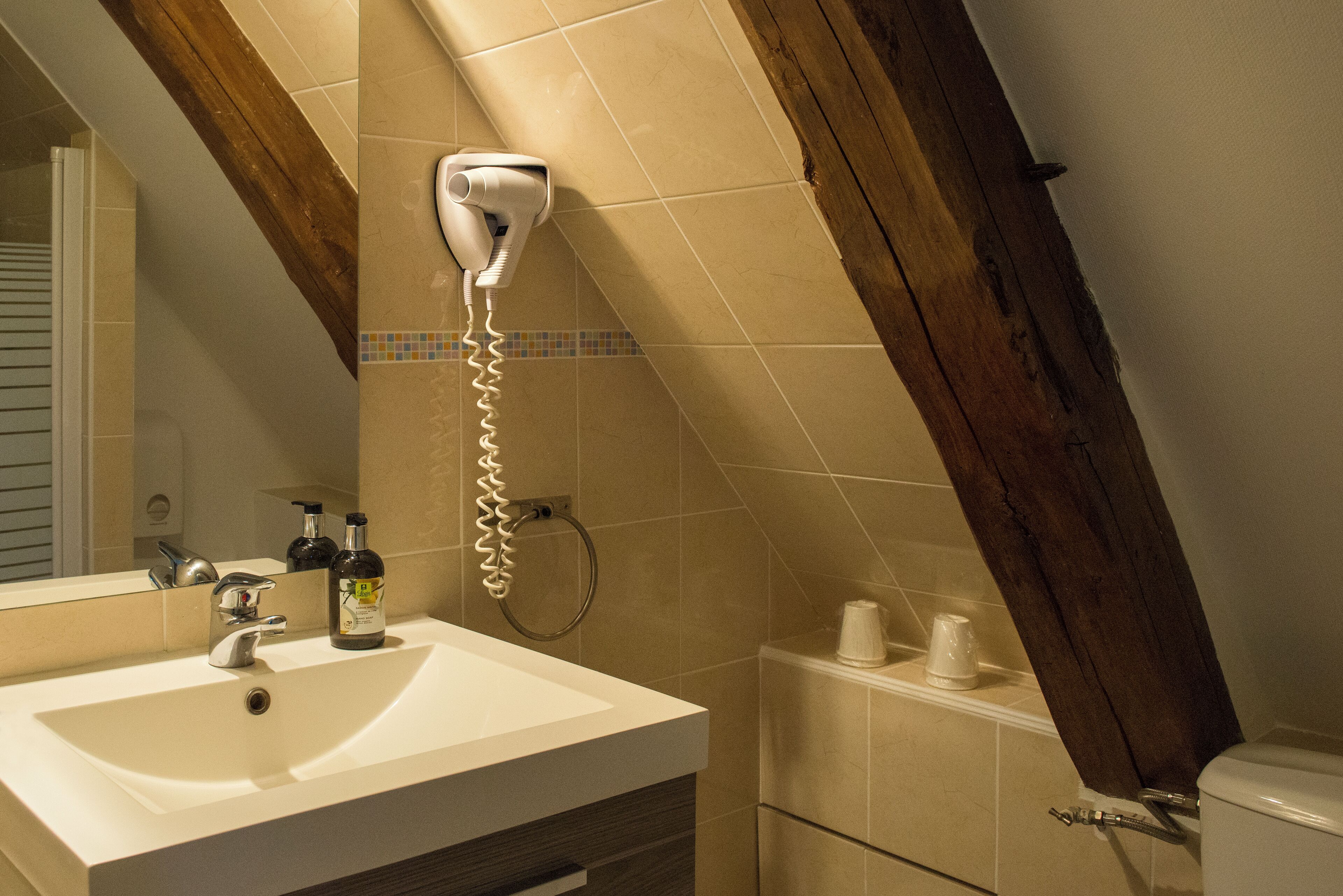 A bathroom with a white sink, a hairdryer mounted on the wall, and a mirror above the sink.