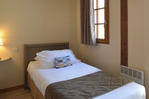 Uma cama bem arrumada com travesseiro estampado, manta acolchoada e mesa de cabeceira com abajur.
