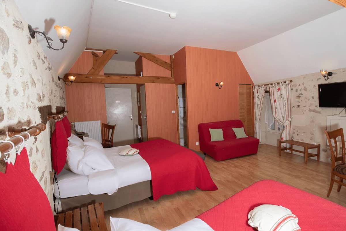 A bedroom with two beds, a red sofa, a wooden table, and a TV mounted on the wall.