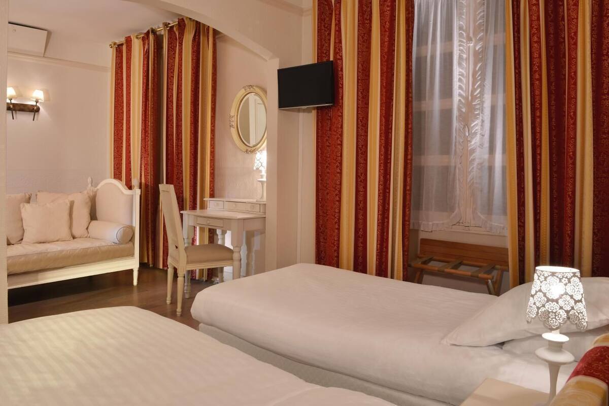 A hotel room with two beds, a desk, a chair, a TV, and curtains.