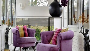 A modern interior with two purple armchairs, a large vase with purple flowers, and a decorative candelabra. - Hermitage (Buzancais)
