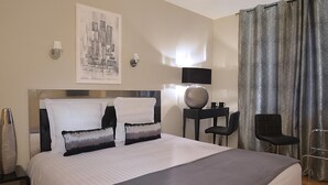 A hotel room with a large bed, a desk with a lamp, two chairs, and a cityscape painting on the wall. - Hermitage (Buzancais)