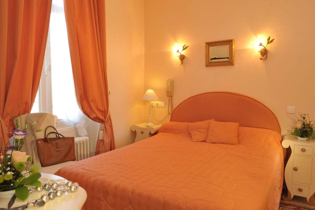 A hotel room with an orange bedspread, a bedside lamp, a telephone, and a mirror on the wall.