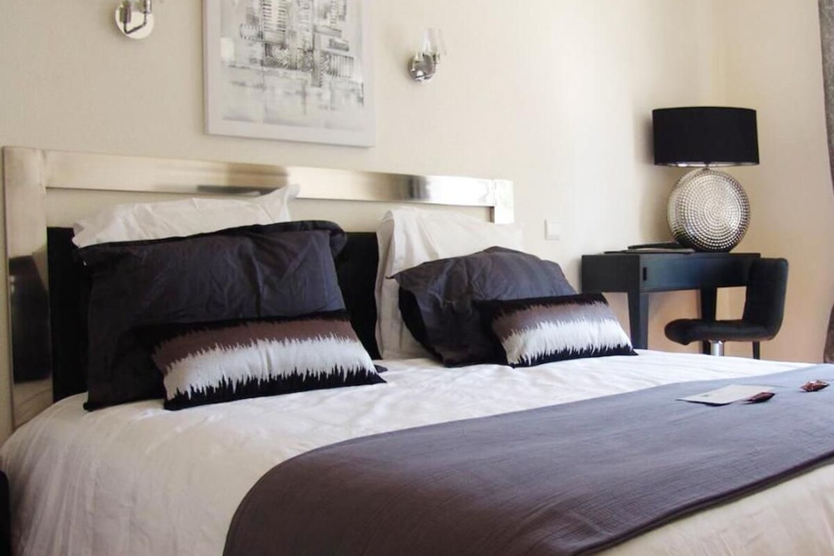 A hotel room with a large bed, two bedside tables, a lamp, and a framed cityscape on the wall.