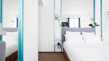 Una habitación de hotel con una cama, una mesita de noche, un espejo y una ventana.