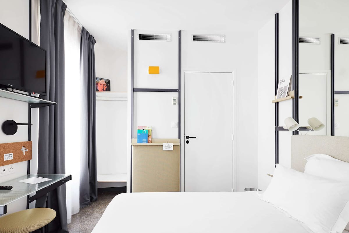 A hotel room with a bed, a desk, a chair, a TV, a wardrobe, and a mirror.