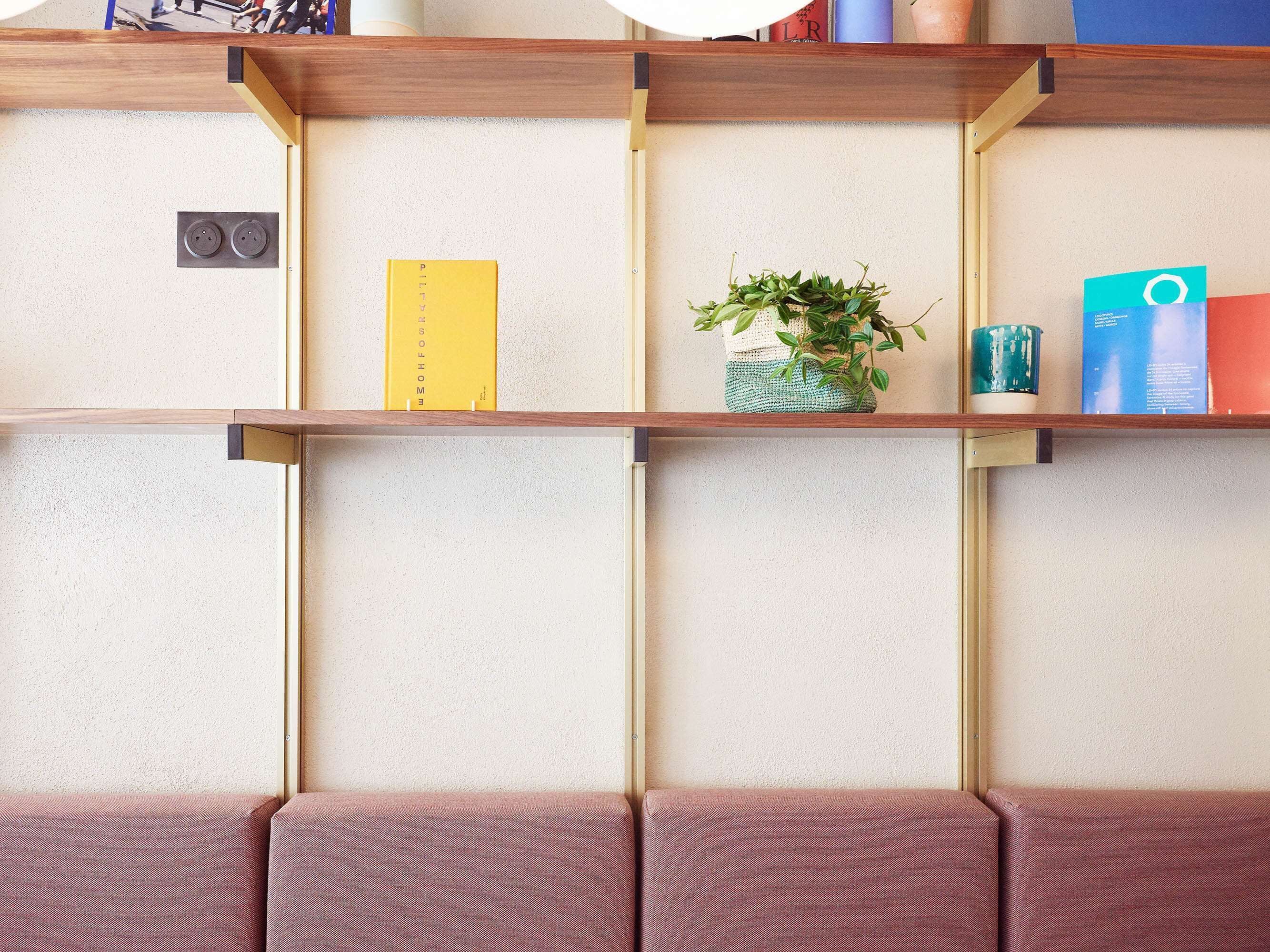 A room with a wooden shelf unit against a textured wall, a small potted plant, and a red couch.