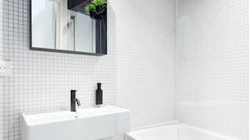 Une salle de bain moderne avec un mur recouvert de carreaux blancs, un lavabo rectangulaire doté d’un robinet noir, un miroir au-dessus du lavabo et une baignoire blanche.