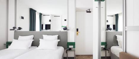 A hotel room with a large bed, a desk, a chair, a TV, and a mirror.
