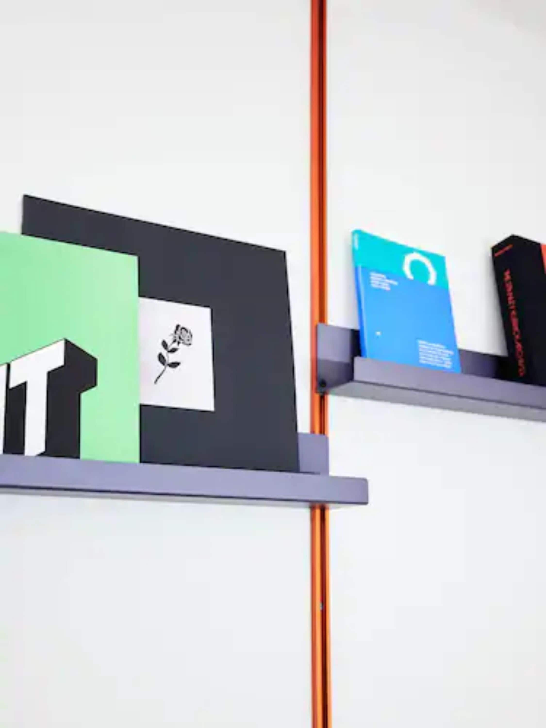 A wall with two shelves holding books and a vertical orange pole.
