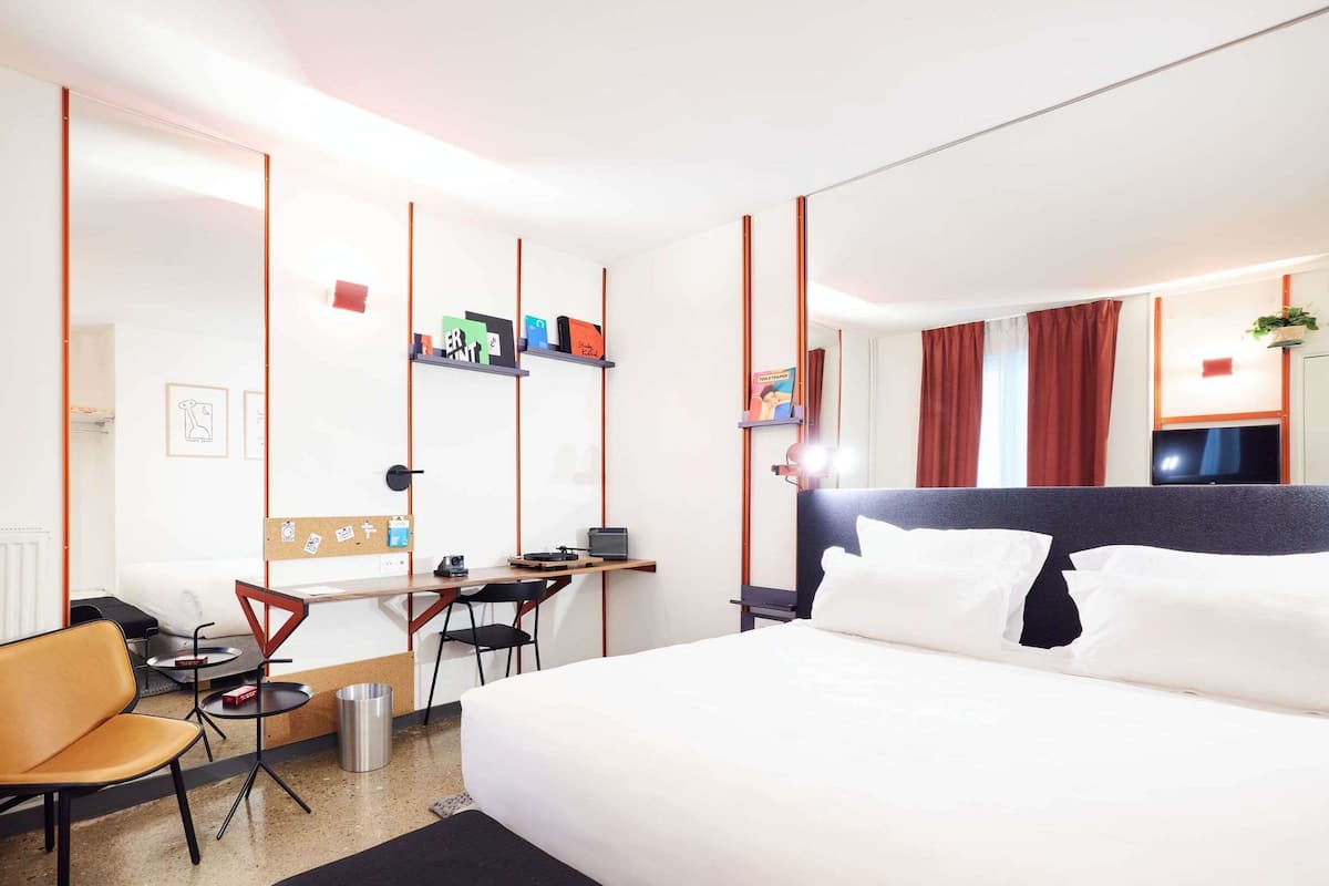 A hotel room with a bed, a desk, a chair, and a radiator.