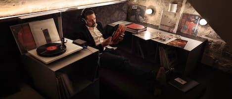 A man sitting at a table with a record player, surrounded by books and framed pictures.