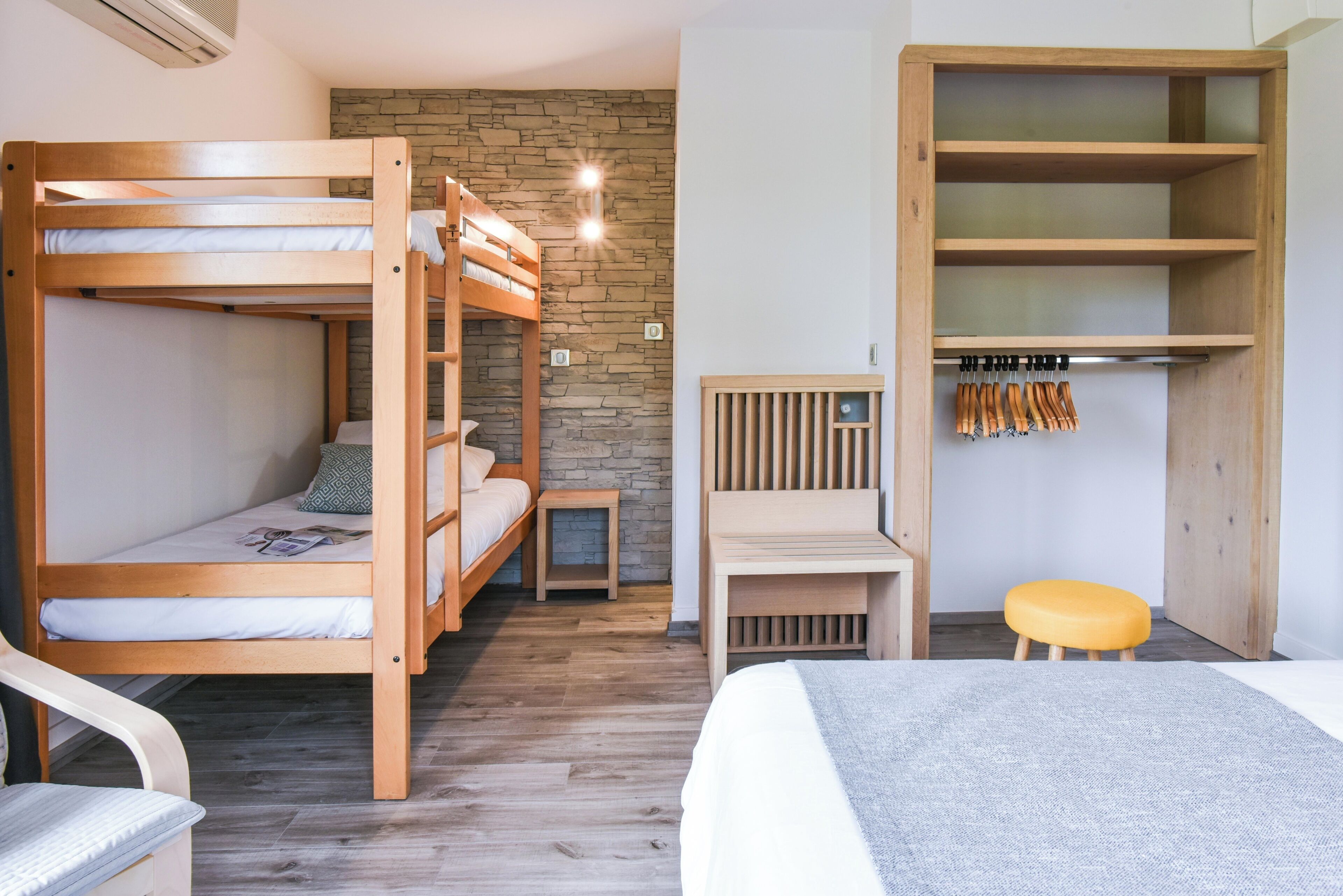 Une chambre avec un lit superposé, un mur en pierre, un bureau et une armoire.