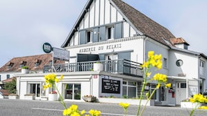 A hotel named 'Auberge du Relais' with a sign indicating it is a hotel and restaurant, a balcony, and a signboard with information.