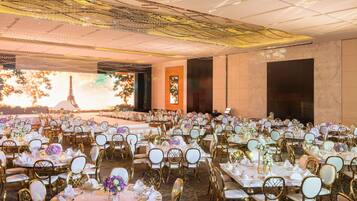 A banquet hall with multiple round tables, each set with white tablecloths, gold chairs, and floral centerpieces.