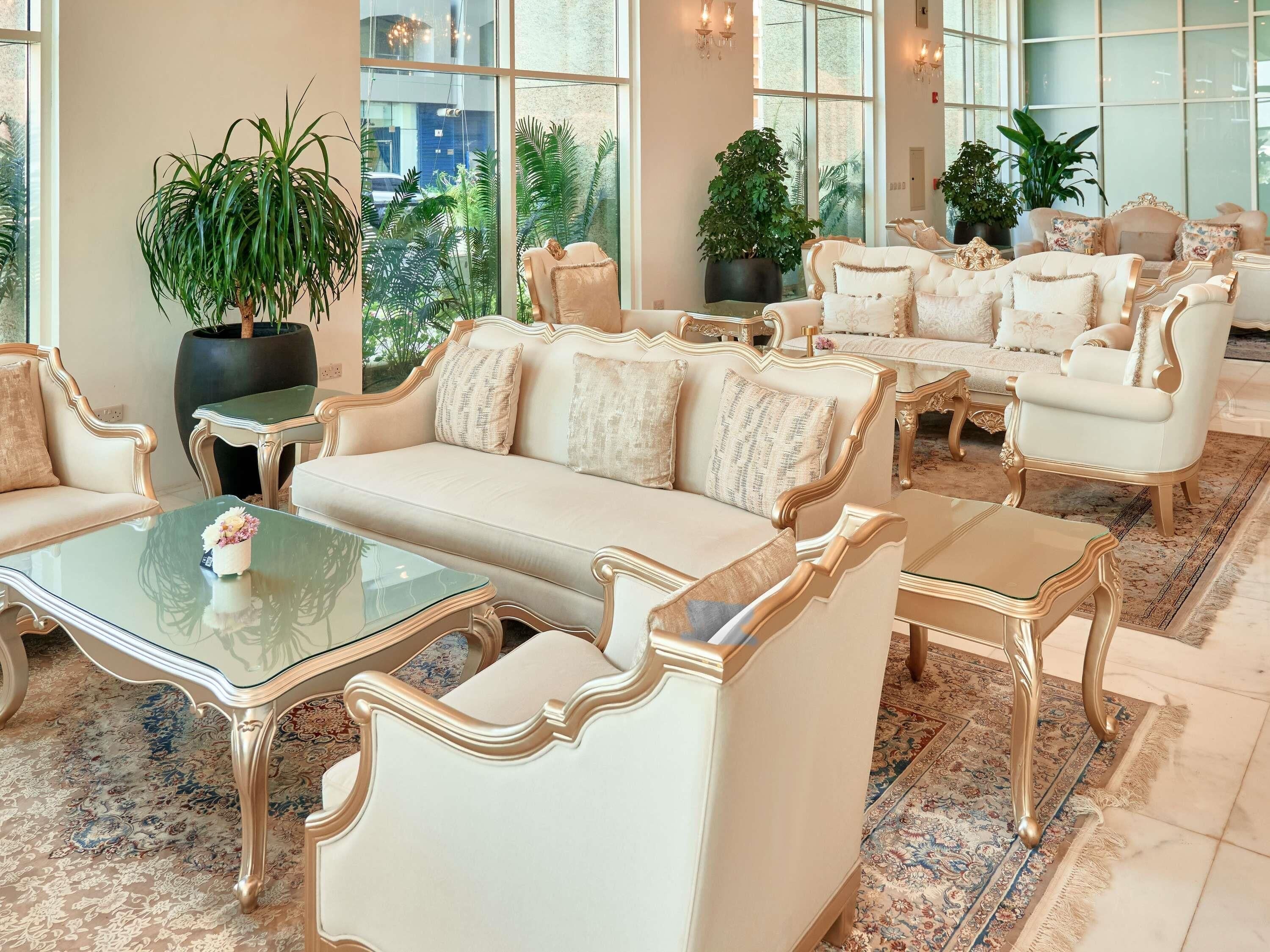 A spacious lounge with a sofa, armchairs, and a coffee table. Large windows offer a view of the outdoors.