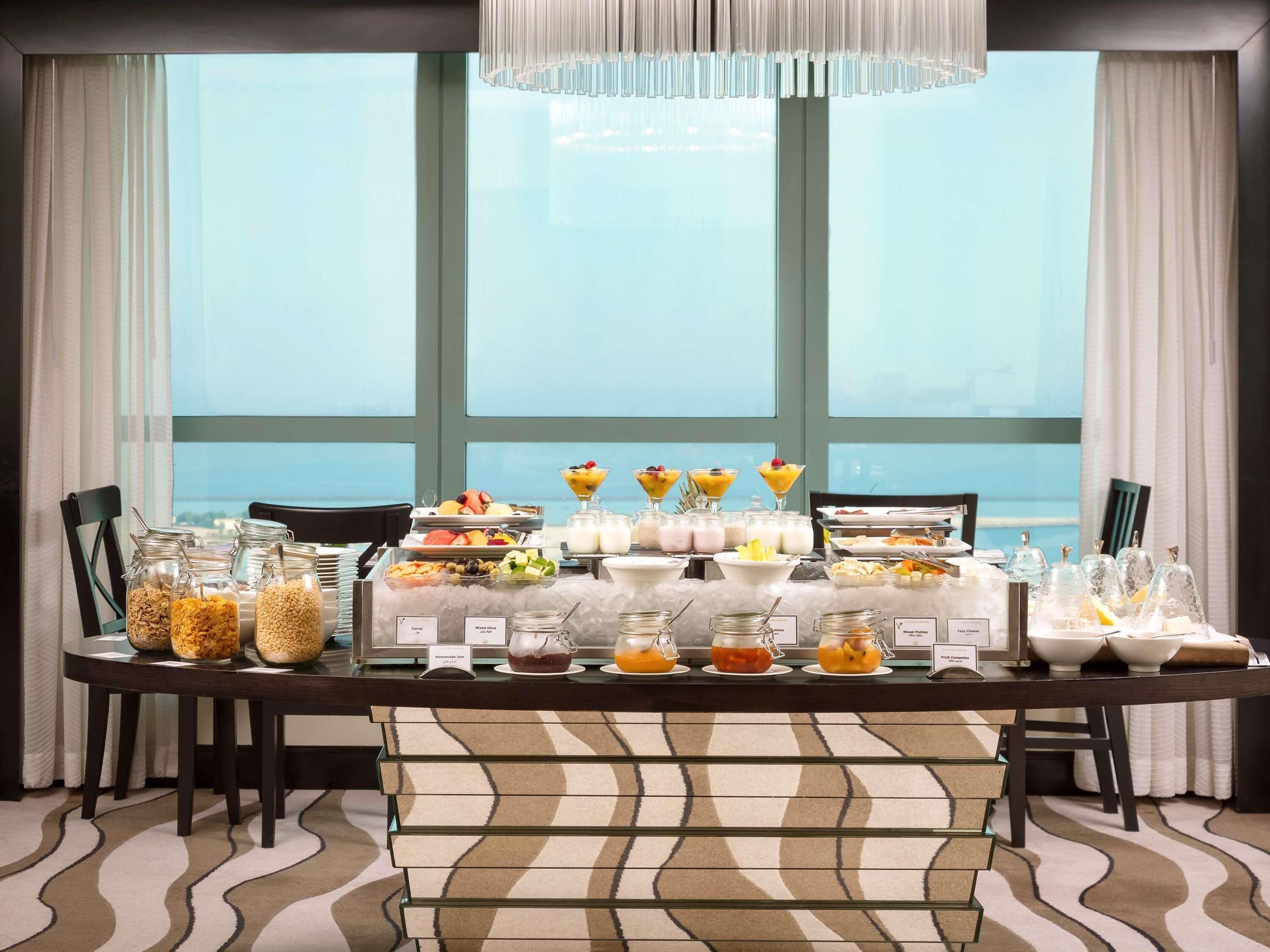 Ein Frühstücksbuffet mit verschiedenen Speisen und Getränken, einer Chandelier und Blick durch große Fenster.