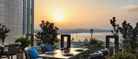 A terrace with a table and chairs, overlooking a body of water and distant hills.