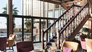 Un área de comedor con vistas a una piscina y palmeras, una escalera de madera y mobiliario moderno.