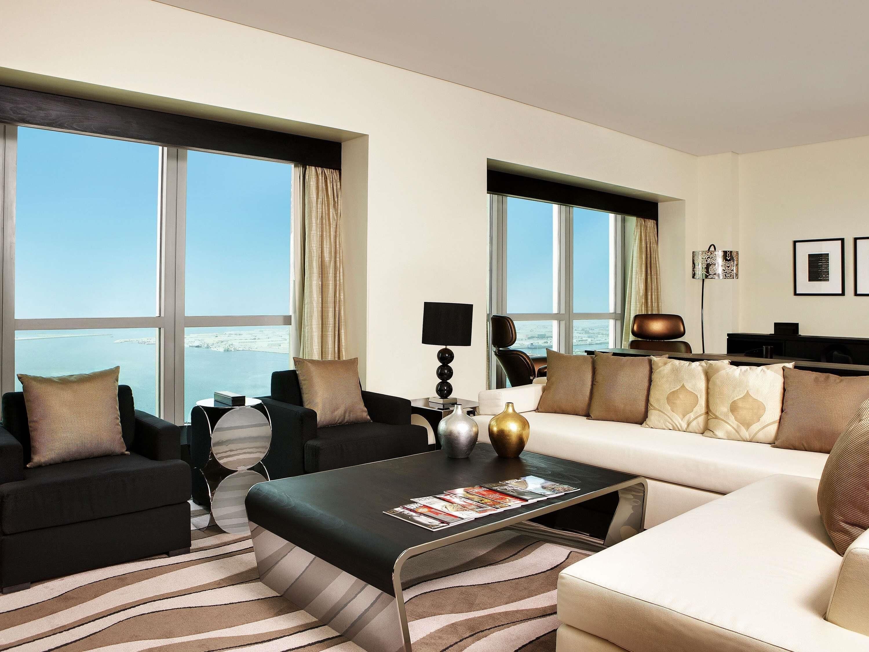 Une chambre d’hôtel moderne, dotée d’un canapé, de fauteuils, d’une table basse et de grandes fenêtres offrant une vue sur la mer.