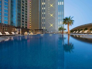 A swimming pool with lounge chairs, a modern building with vertical lines, and palm trees. - Sofitel Abu Dhabi Corniche (Abu Dhabi)