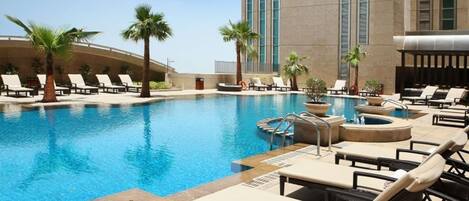 A hotel pool area with lounge chairs, palm trees, and a hot tub.