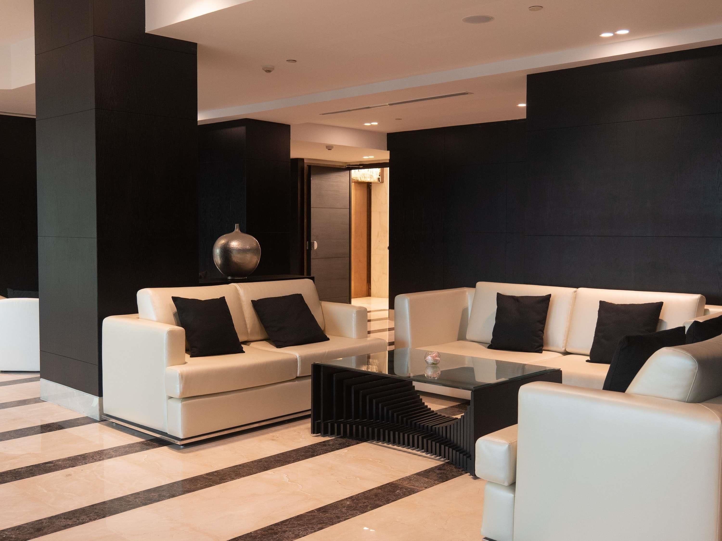 A modern living room with two white sofas, a glass coffee table, and a black accent piece.
