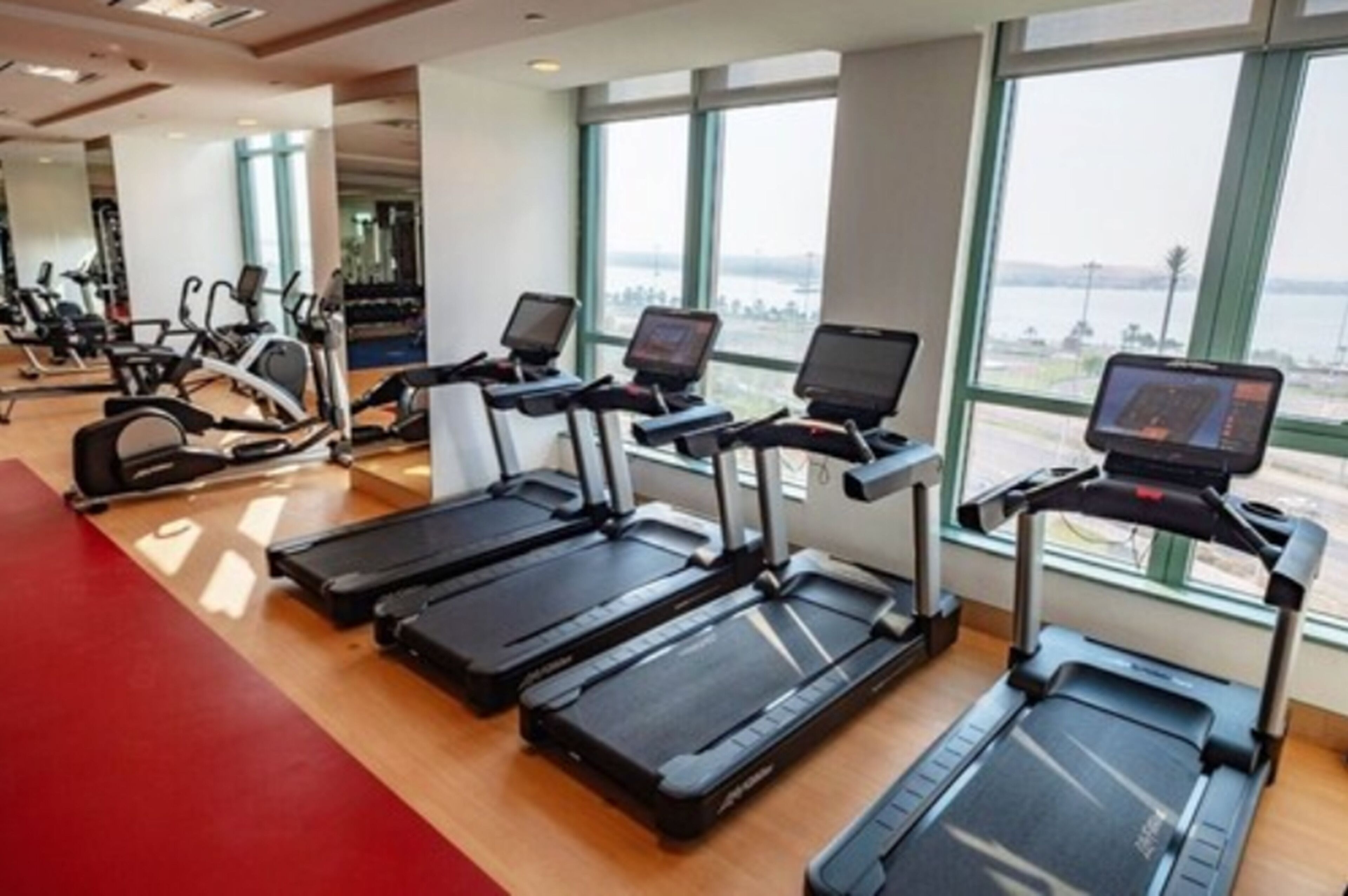 A gym with treadmills and exercise equipment, large windows, and a view of the outdoors.