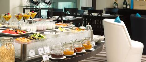 A buffet with various food items and beverages, including fruits, cheeses, and mixed juices.