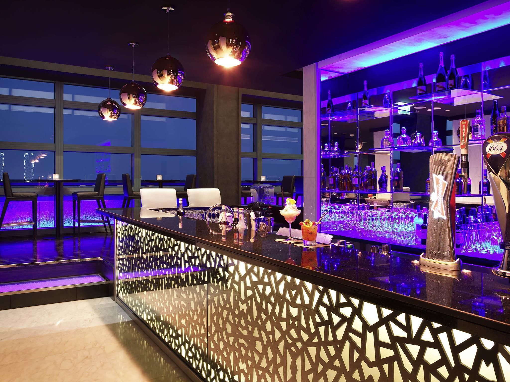 A bar area with a modern design, including a patterned partition, bar stools, and a variety of bottles and glasses.