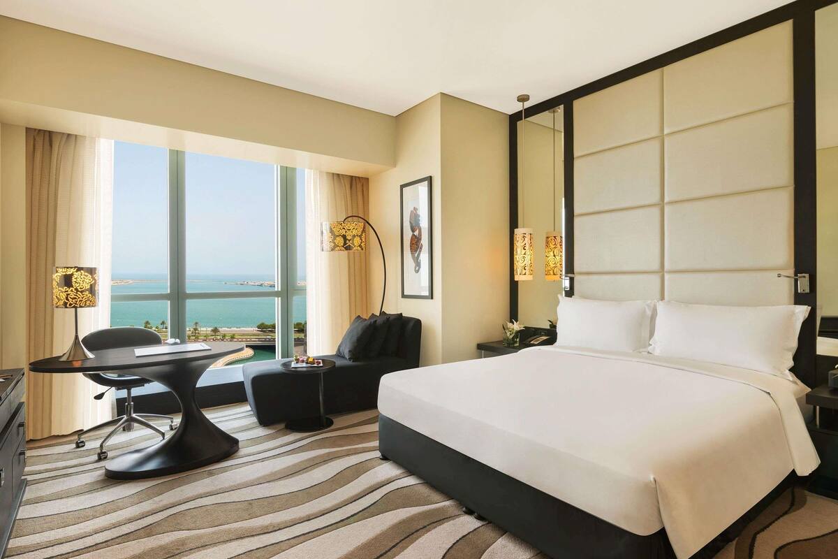A hotel room with a large bed, a desk, a chair, and a view of the sea.