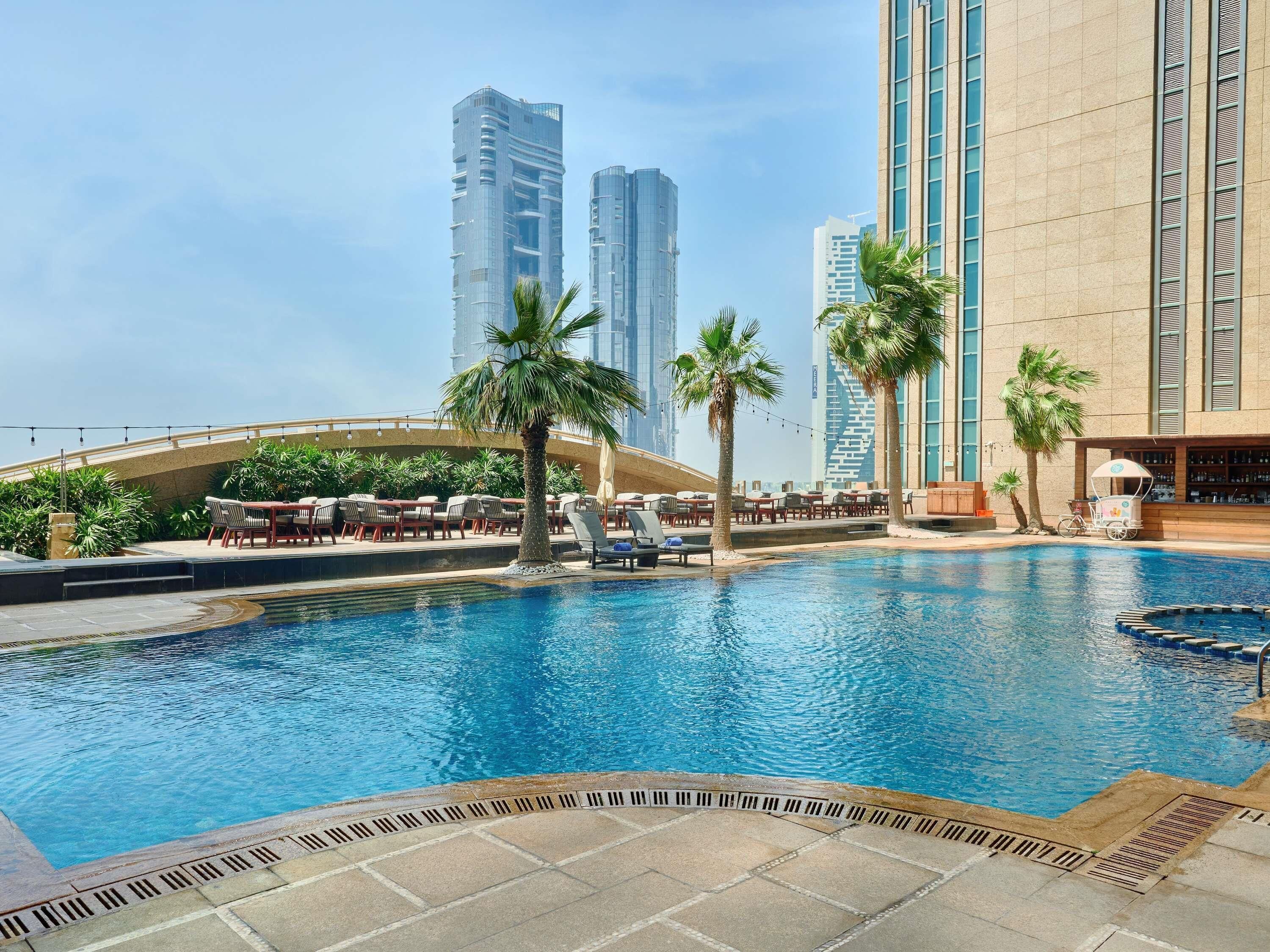 A swimming pool with lounge chairs and palm trees, surrounded by high-rise buildings.