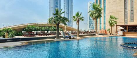 A swimming pool with lounge chairs and palm trees, surrounded by high-rise buildings.