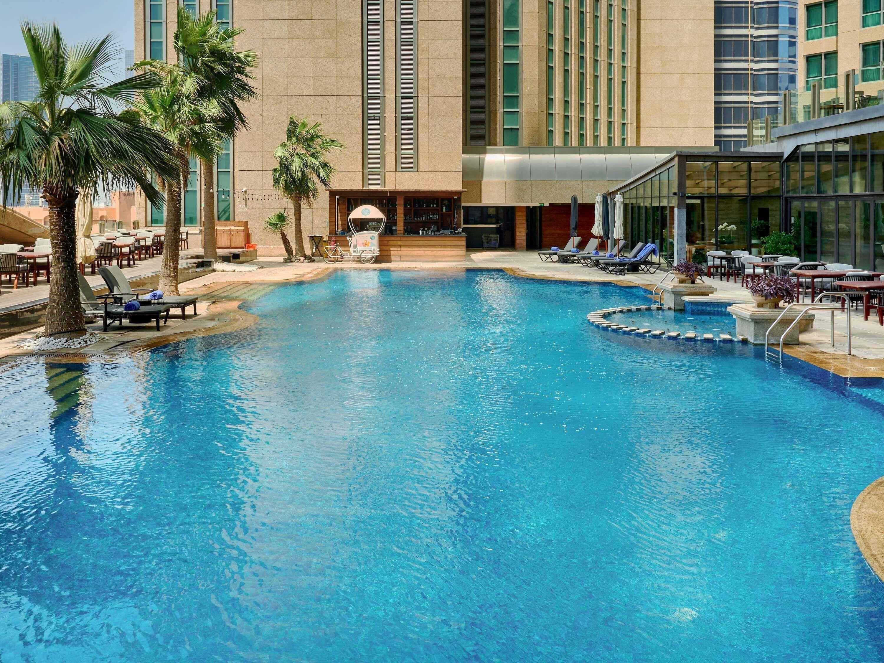 A swimming pool with lounge chairs and palm trees, surrounded by a modern building with large windows.