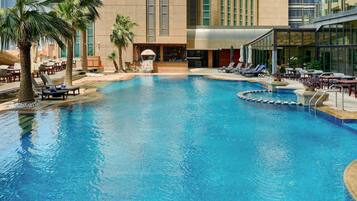 A swimming pool with lounge chairs and palm trees, surrounded by a modern building with large windows.