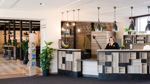 Un área de recepción de diseño moderno, con un mostrador de madera y color negro, lámparas colgantes y plantas en macetas.
