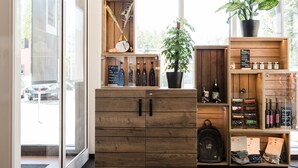 Interior de madera con un ventanal de vidrio que da al exterior, estantes con botellas, una planta en maceta y un letrero con nombres de productos.