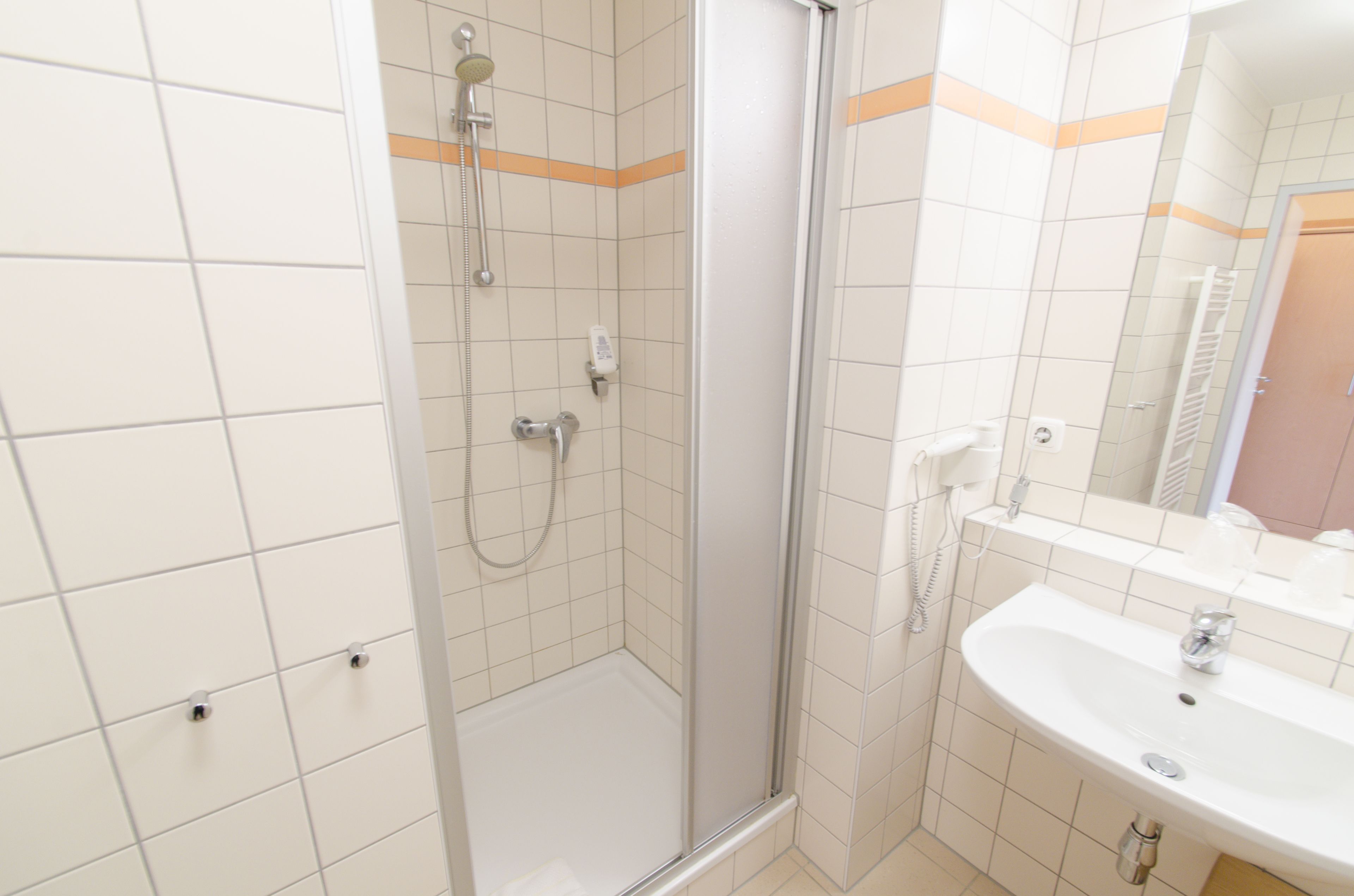 Un baño moderno con ducha envuelta en cristal, un lavabo blanco y un espejo encima.