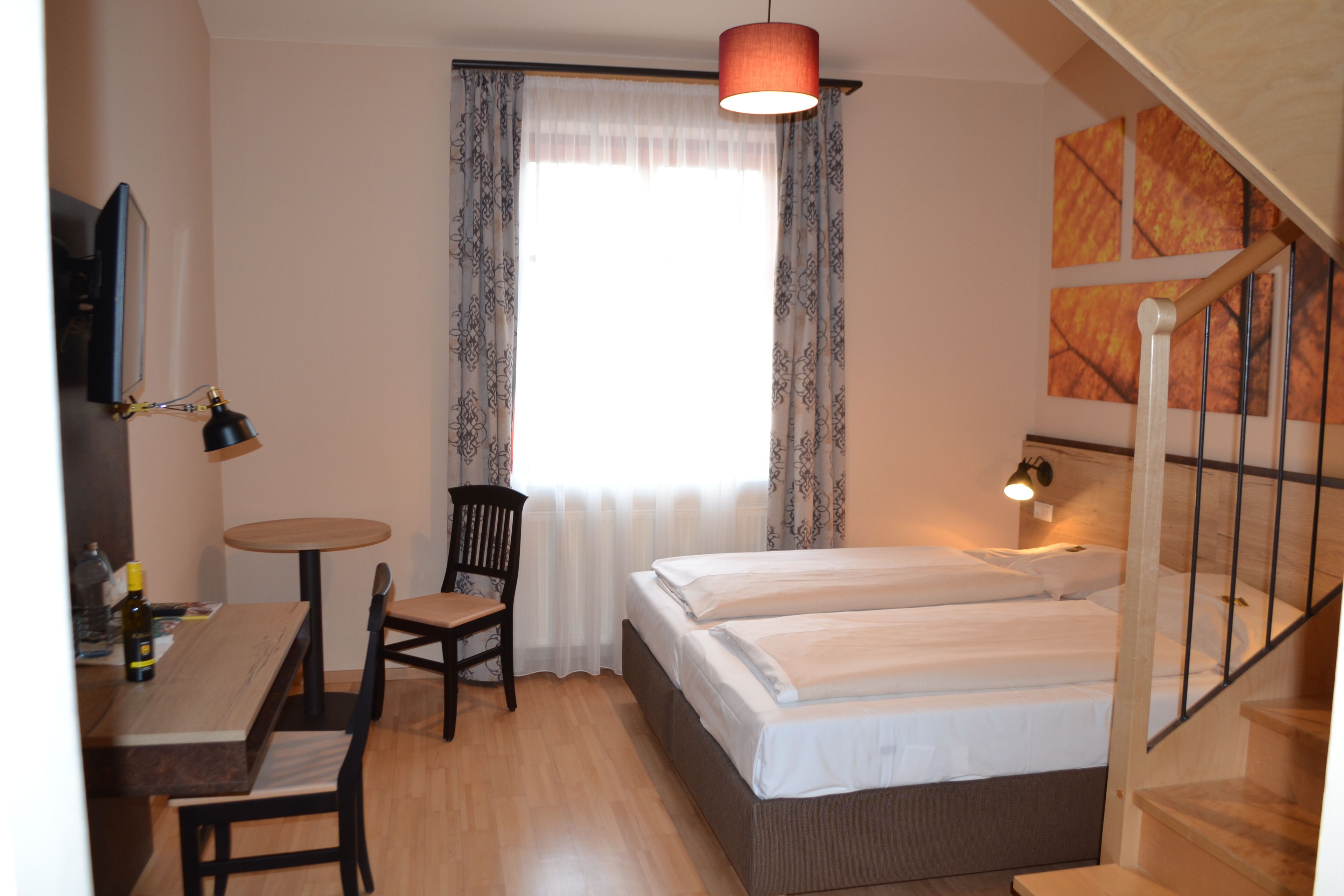 Une chambre à coucher avec un lit double, un bureau avec une chaise, une petite table, une chaise, une fenêtre avec des rideaux et un escalier.