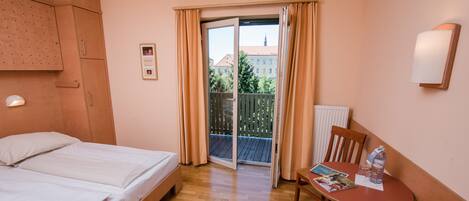 Habitación de hotel con cama, una pequeña mesa con silla, ventana con cortinas y lámpara fijada en la pared.