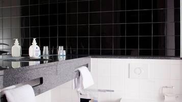 A modern bathroom with a black tiled wall, a white toilet, a sink with a mirror, and a trash bin.