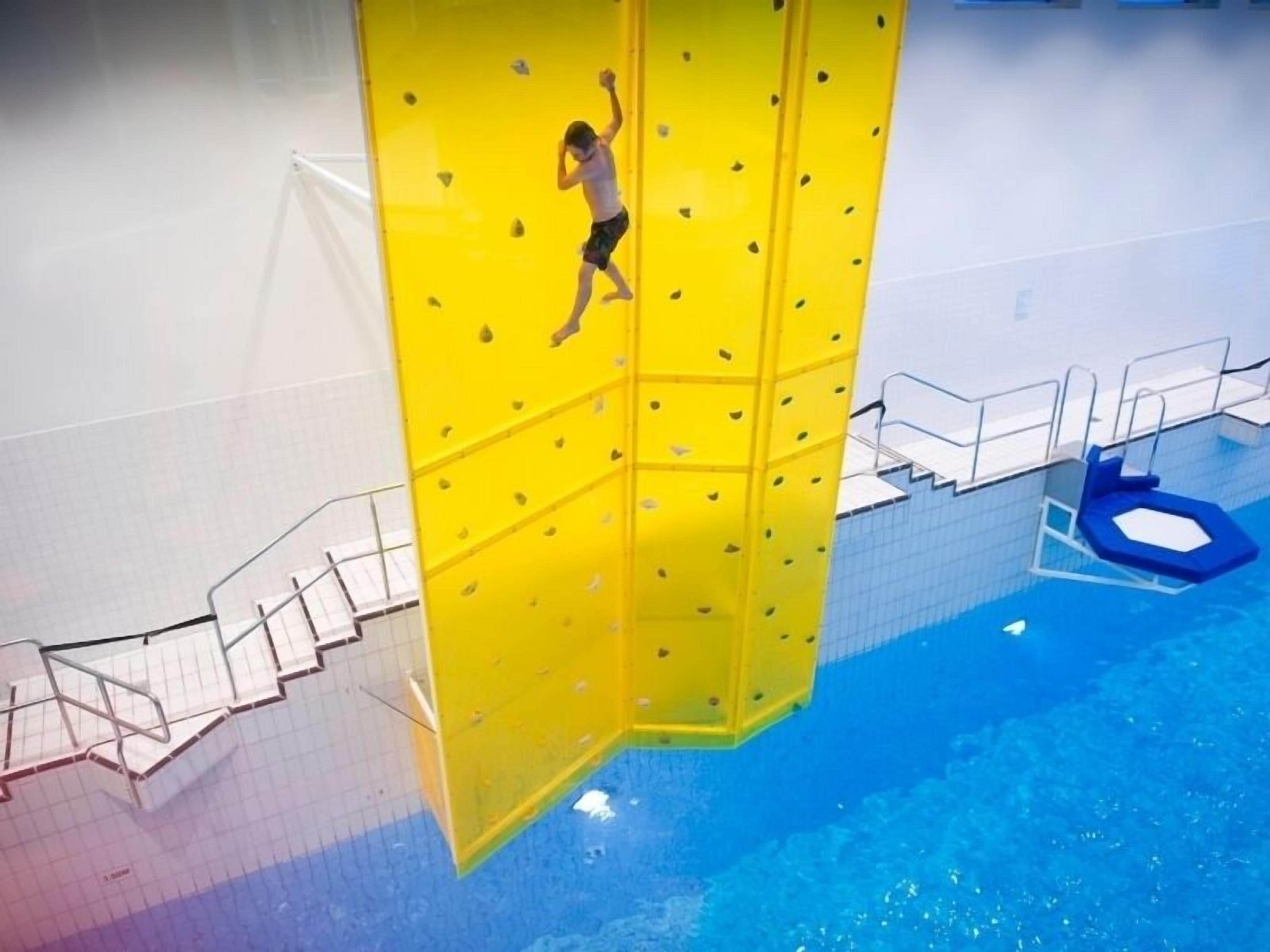 Una persona escalando una pared amarilla en un área de piscina.