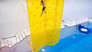 Una persona escalando una pared amarilla en un área de piscina.