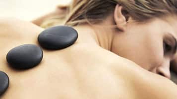 A person receiving a back massage with black stones.
