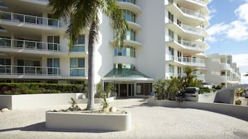 A modern hotel with multiple balconies, a central courtyard with palm trees, and a paved walkway.