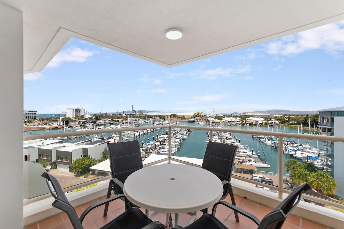 A balcony with a white table and four chairs, overlooking a marina with numerous boats and buildings in the background.