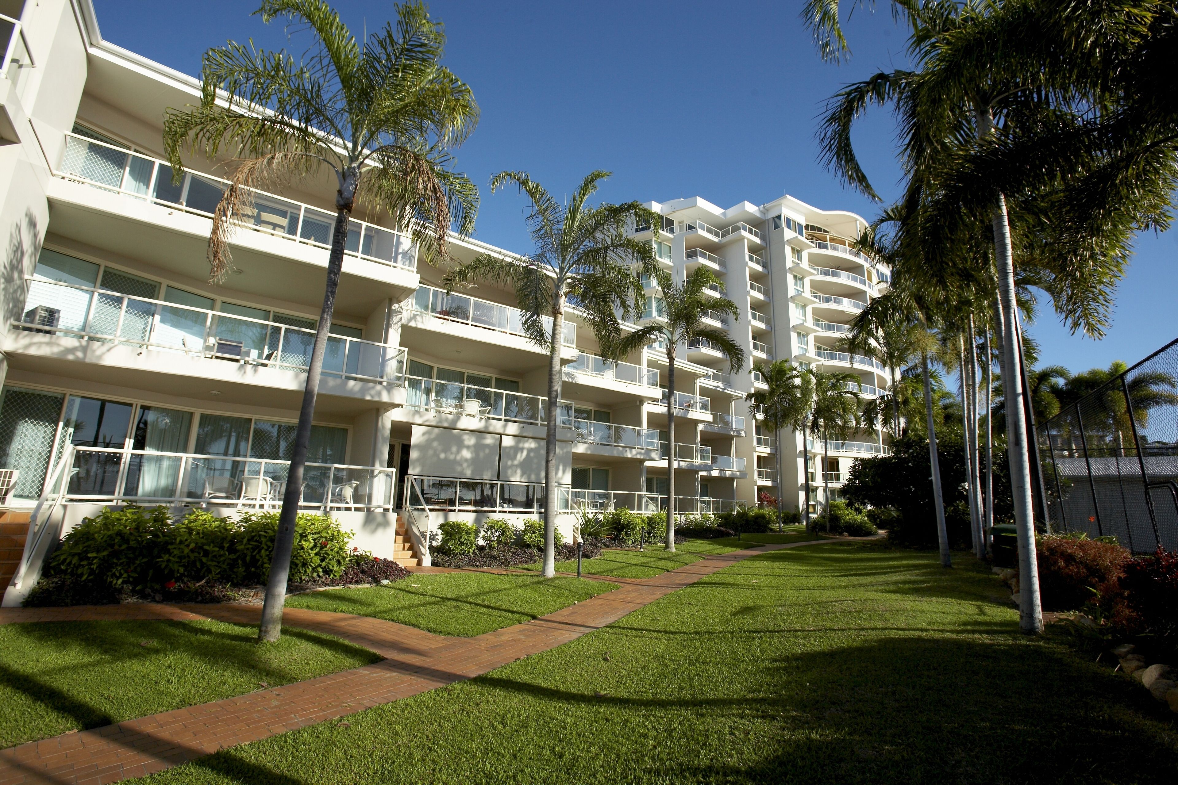 A multi-story hotel with balconies, palm trees, and a well-maintained lawn.