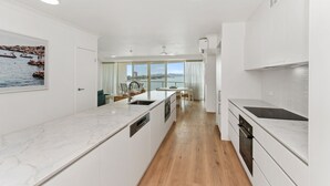 Una cucina moderna con mobili bianchi, un piano di lavoro in marmo e vista sul mare grazie a ampie finestre.