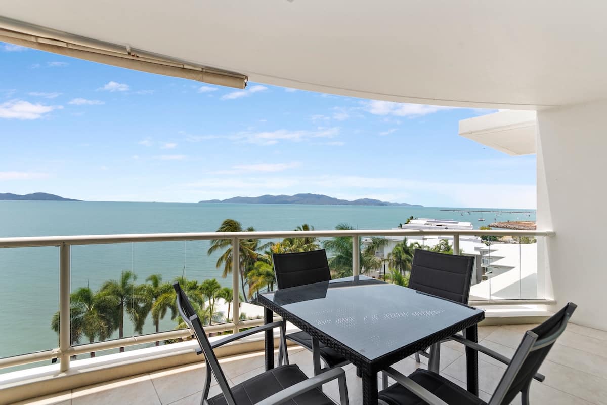 A balcony with a table and chairs overlooking a coastal view.