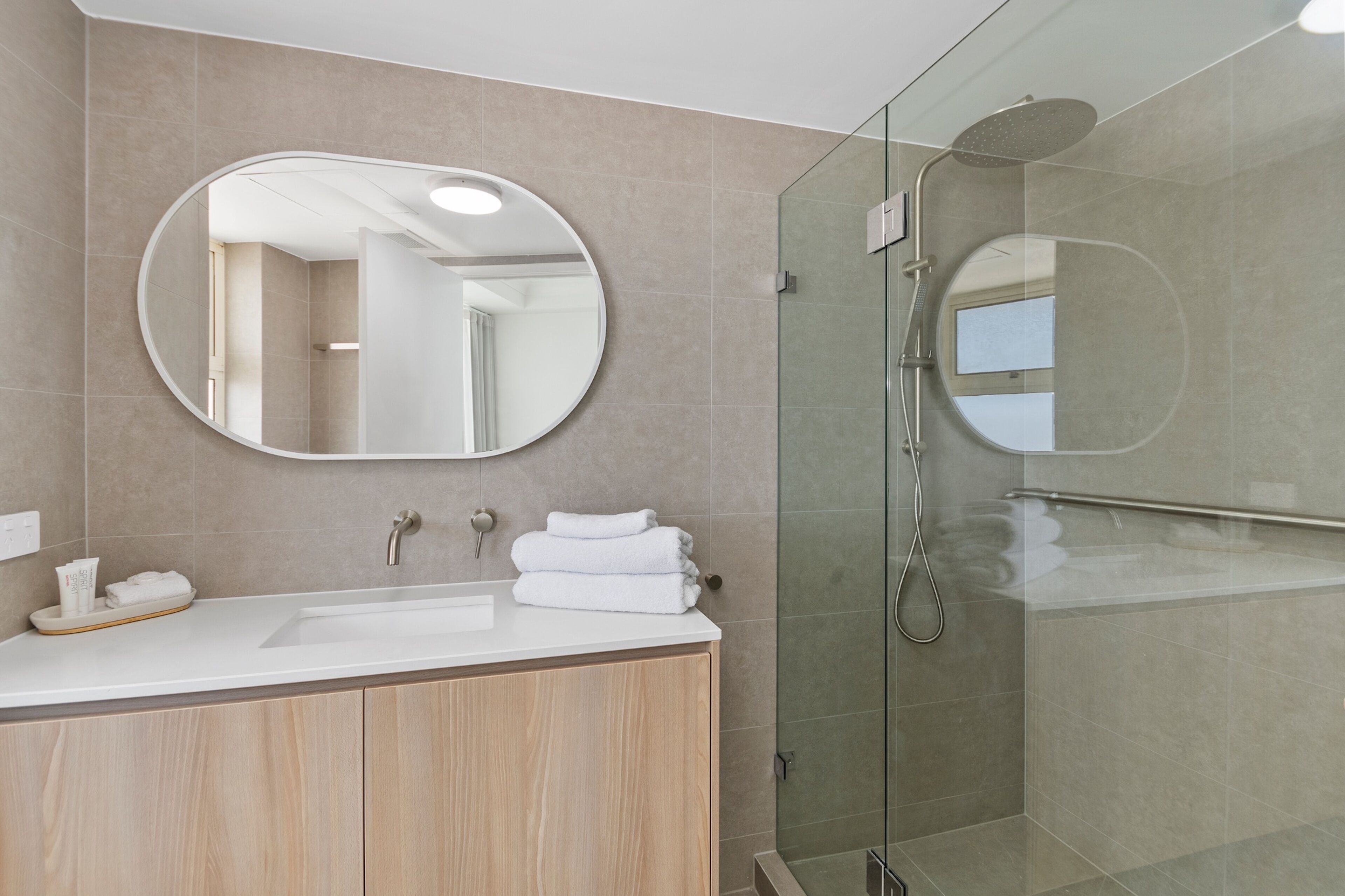 A modern bathroom with a large mirror, a sink, and a glass-enclosed shower.